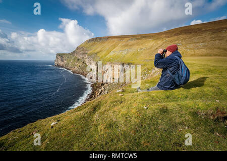A birdwatcher sitting on the top of sea cliffs on Foula, Shetland Stock Photo