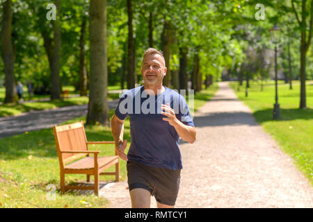 Middle aged man jogging along alley in park on sunny day in a close up view Stock Photo