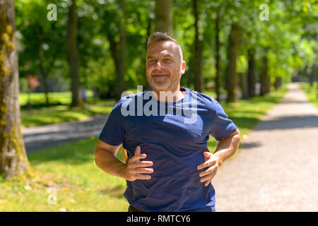 Middle aged man jogging along alley in park on sunny day in a close up cropped view Stock Photo