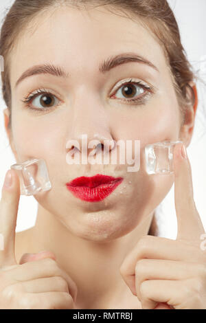 serious young woman applying ice cubes on her face skin, isolated on white background, looking at camera Stock Photo