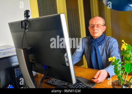 Middle aged man with glasses sitting at desk. Mature man using personal computer. Senior concept. Man working at home office Stock Photo