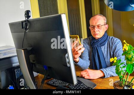 Middle aged man with glasses sitting at desk. Mature man using mobile phone. Senior concept. Man at home office  Stock Photo
