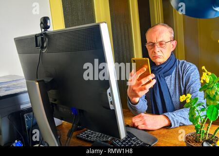 Middle aged man with glasses sitting at desk. Mature man using mobile phone. Senior concept. Man at home office Stock Photo