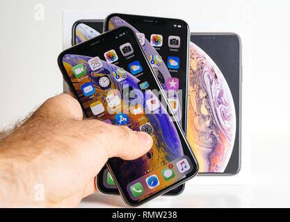 PARIS, FRANCE - SEP 25, 2018: Man hand holding the two new iPhone Xs and Xs Max smartphone model by Apple Computers mobile phone devices after unboxing - isolated on white background Stock Photo