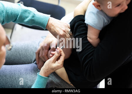 Real baby being vaccinated with a syringe in the thigh by a pediatrician doctor to avoid the spread of diseases. Stock Photo