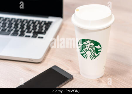 Starbucks coffe cup on the wooden desk in the office next to computer laptop and mobile phone. Slovenia 13.02.2019 Stock Photo