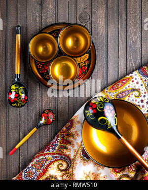 Wooden dishes, painted with floral ornament in the style of Khokhloma Russian wood art on the table with shawl. Stock Photo