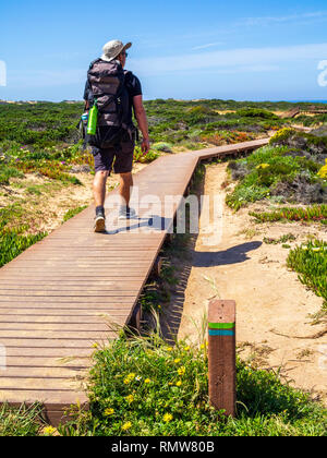 A hiker passes a striped signpost on the Fishermen's Trail between Zambujeira do Mar and Odeceixe in Portugal. The Fisherman's Trail is a four-day wal Stock Photo