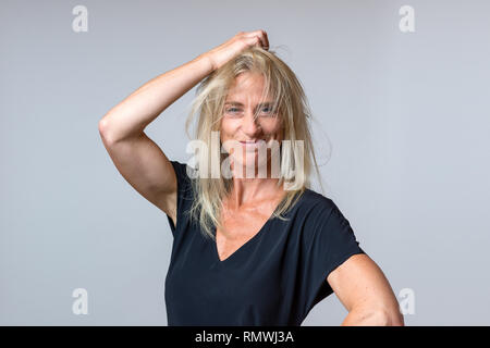 Frustrated woman tearing at her long blond hair, gnashing her teeth and snarling at the camera over grey Stock Photo