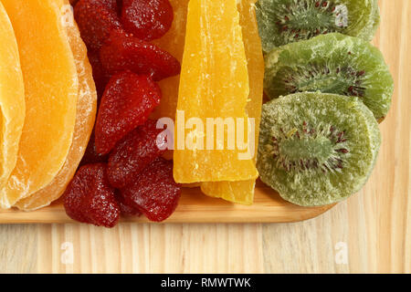 Dried pieces of kiwi, papaya, mango and strawberry fruits, lying on a bamboo plate on a wooden table. Macro. Closeup Stock Photo