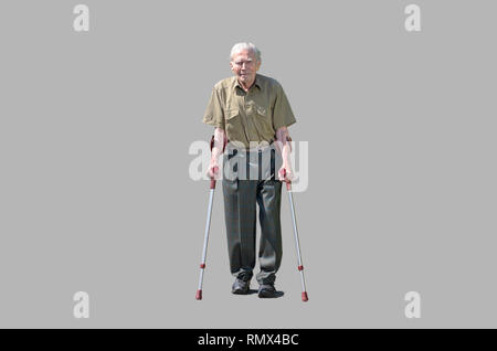 Senior retired man walking on crutches on a walkway between green hedges in a residential suburb approaching the camera front on Stock Photo