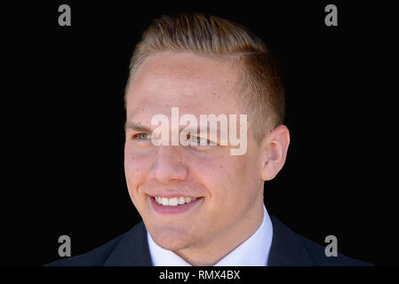 Smiling handsome young businessman in suit and tie looking off to the side with a quiet smile of satisfaction against black background Stock Photo