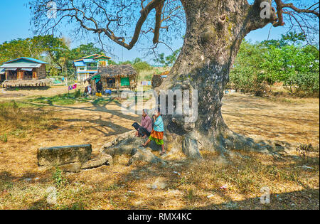 DAR PEIN, MYANMAR - FEBRUARY 15, 2018: The villagers sit under the old tree by the railroad with a view on the stilt huts on the background, on Februa Stock Photo