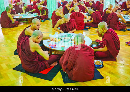 BAGO, MYANMAR - FEBRUARY 15, 2018: The bhikkhu monks sit on the floor at the table in dining hall of Kha Khat Waing Kyaung Monastery and have the lunc Stock Photo