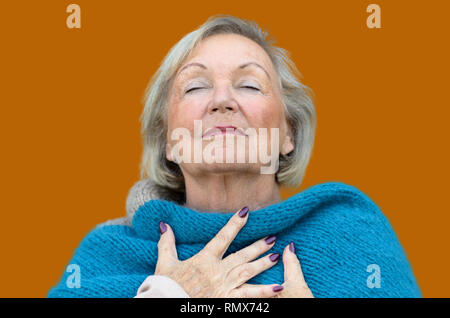 Attractive senior woman savoring the moment standing with her eyes closed and head tilted back with a serene expression as she clasps her chest with h Stock Photo
