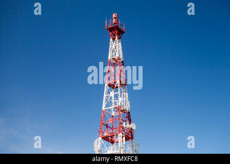 Red white telecommunication tower with radio devices over blue sky background Stock Photo