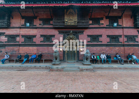 PATAN SQUARE, KATHMANDU, NEPAL-CIRCA 2013 : Unidentified Nepalese men sit and watch people walk by an ancient temple in Patan Square, Nepal. Stock Photo