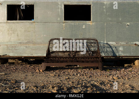 An old, abandoned and wrecked vintage Airstream trailer with a rusted out sofa outside. In the desert of West Texas. Stock Photo