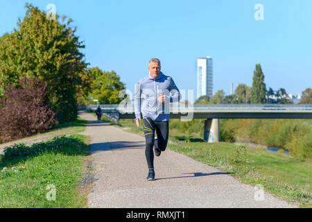 Front view of gray man wearing sportswear running along river Stock Photo