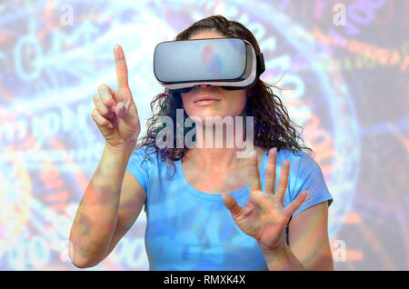 Woman in blue t-shirt using VR interface in 3D goggles, pointing with her index finger on invisible button. Front half-length portrait against abstrac Stock Photo