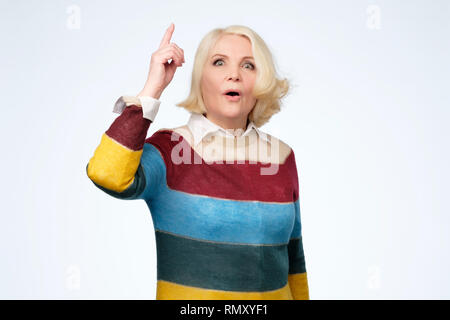 Cheerful senior blond woman pointing up and looking at camera Stock Photo