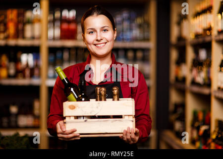Image of happy woman with wooden box with bottles in her hands in wine shop Stock Photo