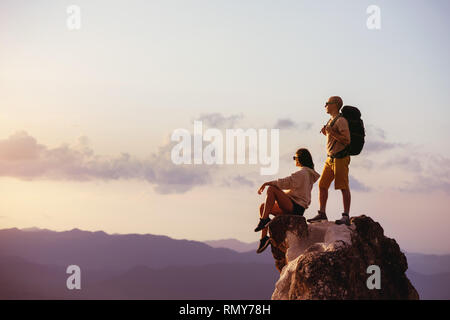 Couple of backpackers relaxing on big rock at sunset time. Space for text Stock Photo