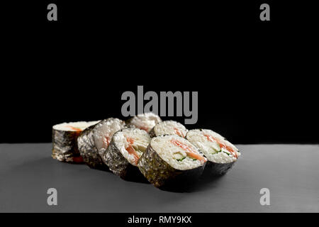 Sake maki rolls with kappa, white rice, wrapped in nori. Sushi with salmon and cucumber served on black stone slate plate. Stock Photo