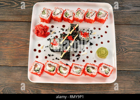 Philadelphia rolls with salmon, cream cheese and cucumber. Uramaki sushi set decorated with mayo, wasabi and pickled ginger, covered in red tobiko roe, presented on white plate. Stock Photo