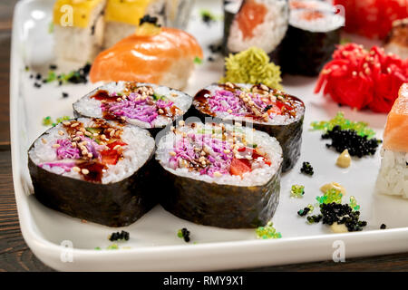 Vegaterian maki close up, on white plate with other kinds of sushi. Veggie rolls with vegetables, violet cabbage, cucumber, served with sause, pickled ginger and wasabi. Stock Photo