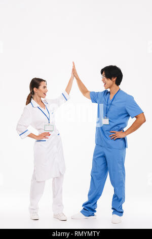 Happy doctors couple wearing uniform standing isolated over white background, giving high five Stock Photo