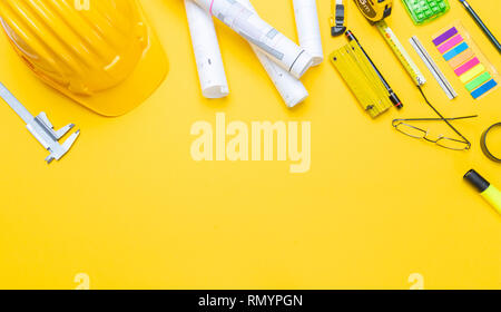 Architect engineer workplace, construction site desk. Project blueprints, hard hat and engineering tools on yellow, copy space, top view Stock Photo