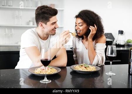Beautiful young multiethnic couple having a romantic dinner at home, drinking red wine and eating pasta Stock Photo