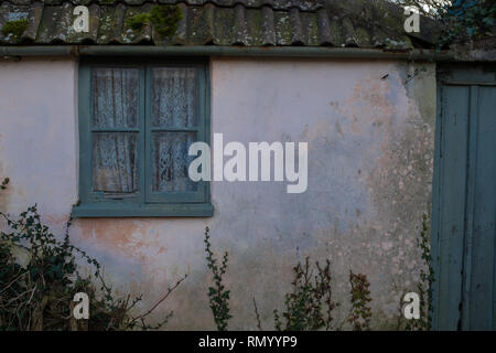 Cottage needs some love, faded blue paint around the window and gate of a rural cottage, small amount of foliage Stock Photo