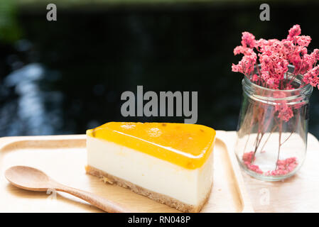 Passion fruit cheesecake serve on wood tay and wooden table with dried flower vase dark background Stock Photo