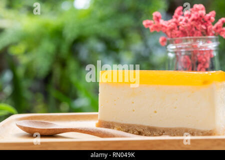 Passion fruit cheesecake serve on wood tay and wooden table with dried flower vase green nature background Stock Photo