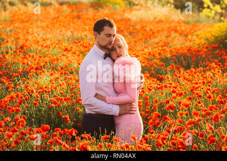 Man and woman embracing in poppy field on the dusk,  countryside Malta Stock Photo