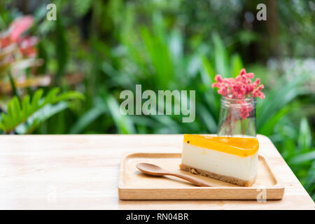Passion fruit cheesecake serve on wood tay and wooden table with dried flower vase green nature background Stock Photo
