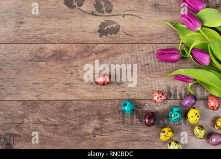 Easter quail eggs - Pastel colored. Beautiful spring flowers - purple tulips on a wooden background. Floral frame with stunning flowers. Copy space Stock Photo