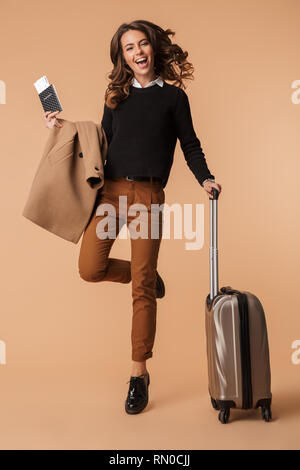 Image of a happy cute amazing young woman posing isolated holding passport with tickets and suitcase. Stock Photo