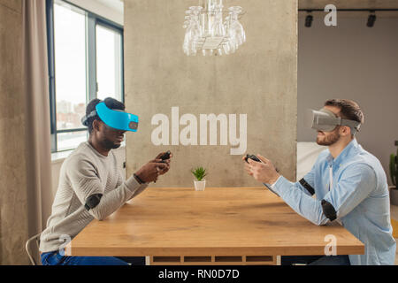 Young caucasian and african male web designers getting experience in working with 3D virtual reality glasses in apartment Stock Photo