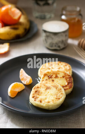 Vegetarian breakfast of quark pancakes with honey, fruit and coffee with milk. Rustic style, selective focus. Stock Photo