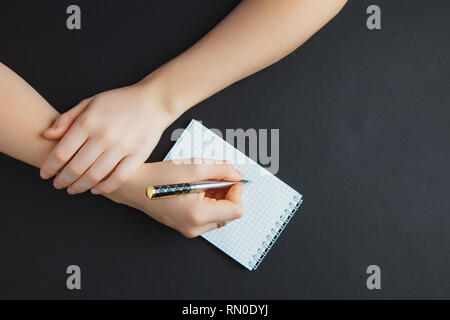A female hands hold a book spread on the wooden desk with pen, top view at the studio. Stock Photo