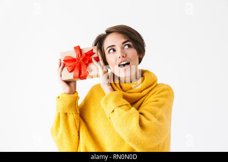 Happy cheerful girl wearing hoodie standing isolated over white background, holding gift box Stock Photo