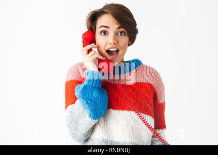 Happy cheerful girl wearing sweater standing isolated over white background, talking on a landline phone Stock Photo
