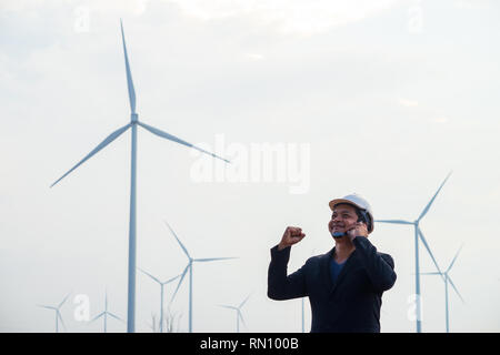 Successful asian engineer man standing and using smartphone with wind turbine. Stock Photo