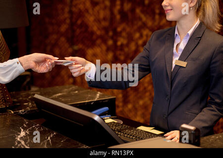 Close up of female hands with blank white badge arriving to hotel, gives credit card to female receptionist, checking in the hotel. Stock Photo