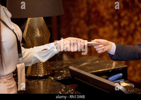 Business woman with blank white badge mockup arriving to hotel, gives credit card to hotel manager for room reservation, close up. Stock Photo