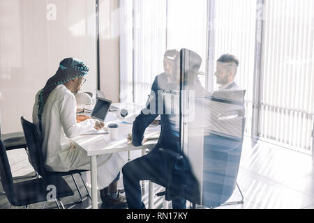 Multiracial team of business partners of different age interacting in boardroom of modern spacious and well-lit office, being viewed through transpare Stock Photo
