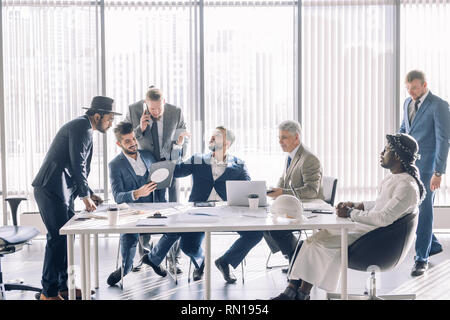 Smiling confident executive in white shirt sitting with laptop at meeting table with business partners team, discussing the working issues. Stock Photo